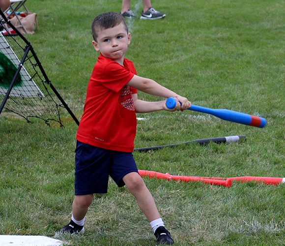 Little boy in red t-shirt hitting wiffle ball.